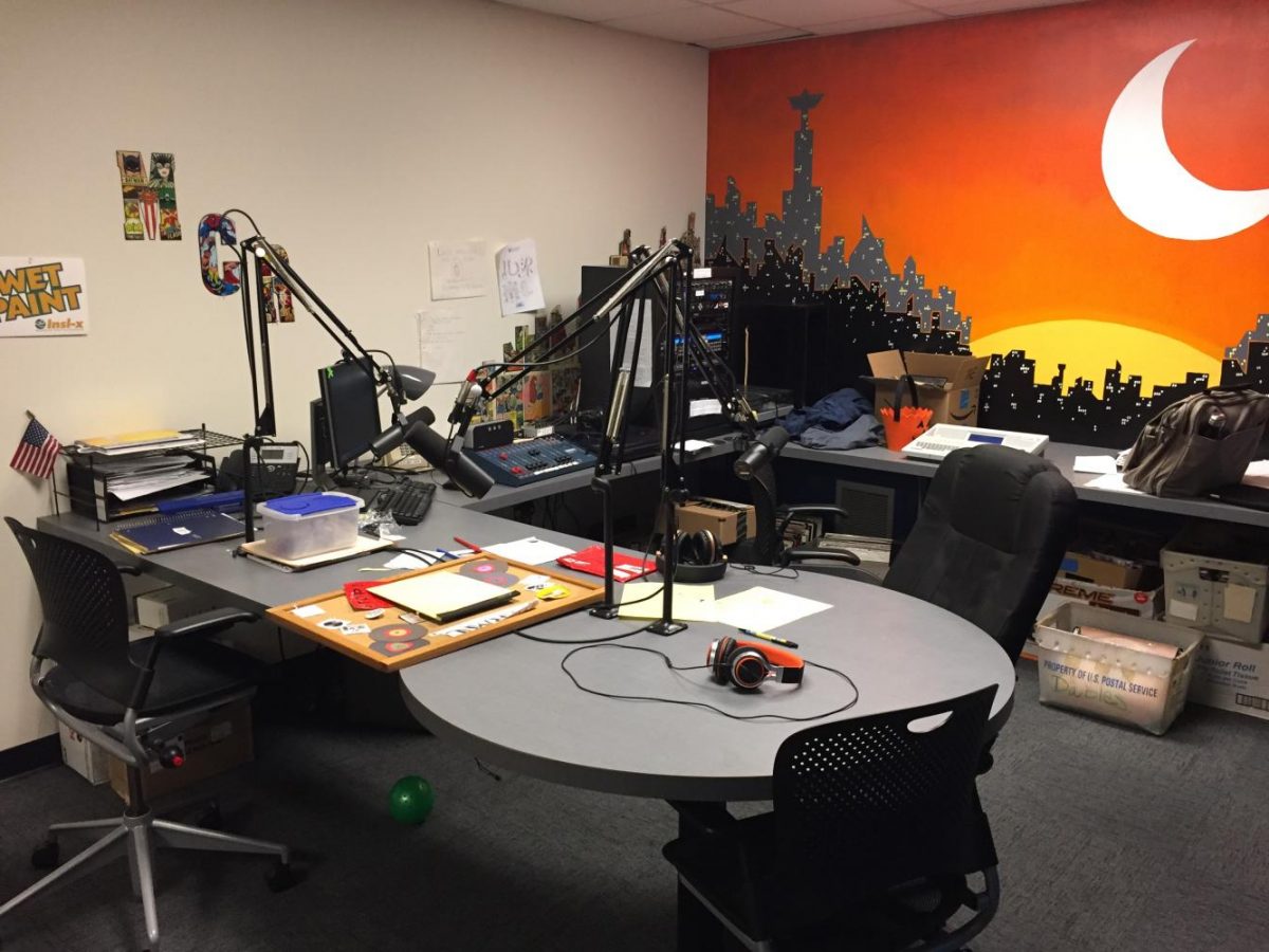 Picture features the radio station with a kidney shaped table with hanging microphones.